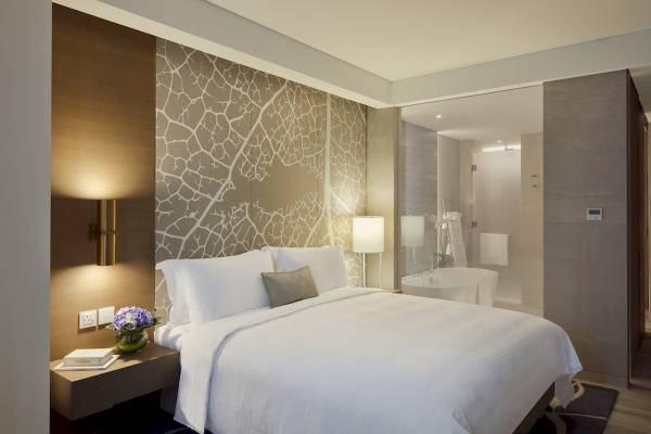Schlafzimmer im Al Bandar Rotana mit Bett, Nachttisch, Lampen und Badezimmer mit Badewanne