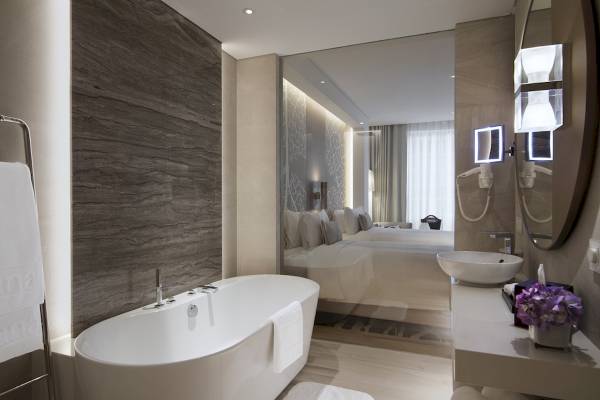 Badezimmer im Al Bandar Rotana Hotel mit Badewanne, Waschbecken und Spiegeln.