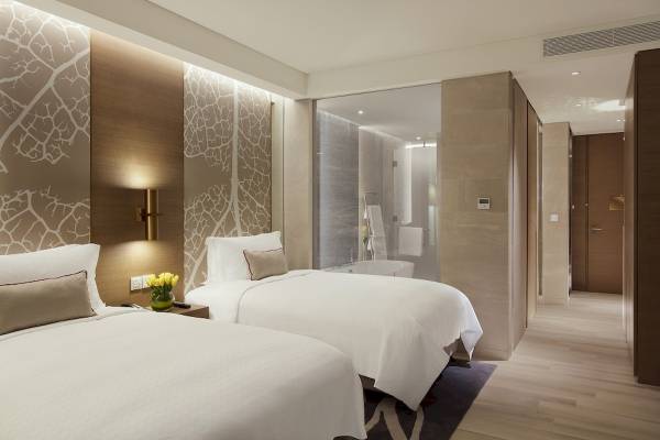 Zwei Doppelbetten im Hotelzimmer von Al Bandar Rotana mit weißen Laken und Kissen, umgeben von modernen Wandverkleidungen.