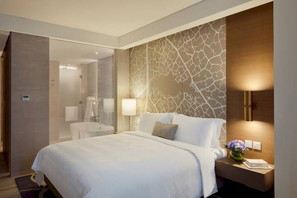 Schlafzimmer im Al Bandar Rotana Hotel mit einem großen Bett, weißem Laken, Kissen, Lampen und einem Nachttisch.
