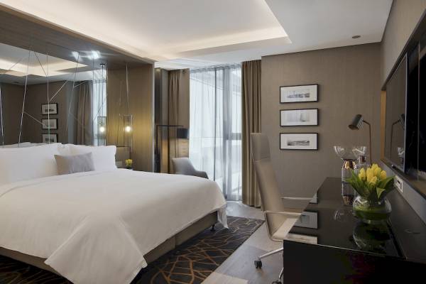 Schlafzimmer im Al Bandar Rotana Hotel mit einem großen Bett, Spiegel, Deko und Schreibtisch.