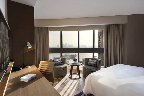 Hotelzimmer im Al Bandar Rotana mit Bett, Sesseln, Tisch und Ausblick auf die Stadt.