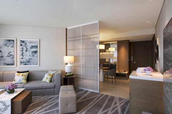 Wohnzimmer-Innenansicht des Al Bandar Rotana Hotels mit grauem Sofa, Tisch, Lampen und Dekoration.