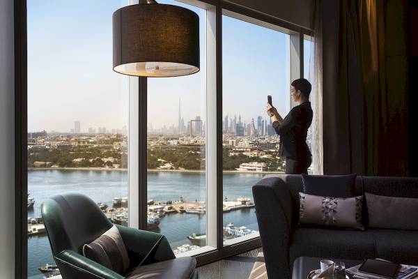 Frau im Al Bandar Rotana Hotel, die vom Fenster aus die Stadt und das Meer fotografiert.