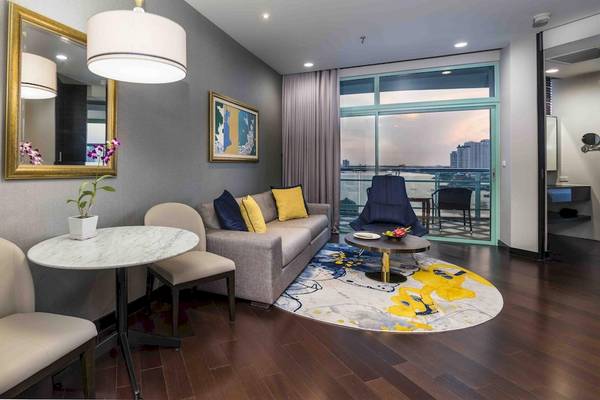 Wohnzimmer des Chatrium Hotel Riverside Bangkok mit Couch, Tischen und Aussicht auf die Stadt.