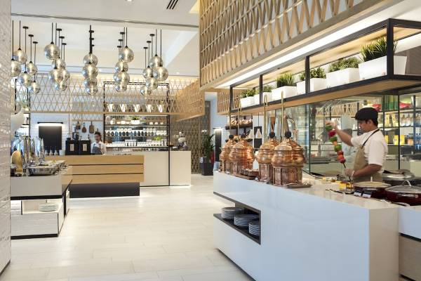 Speisesaal des Al Bandar Rotana Hotels mit Buffet und Köchen, die Speisen zubereiten.