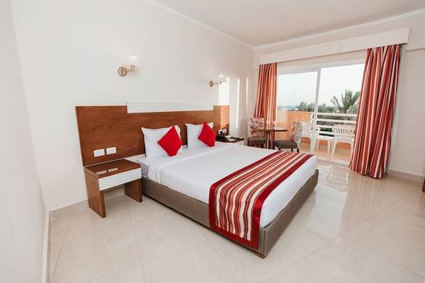 Ein modernes Hotelzimmer im Golden Beach Resort mit einem großen Bett, roten Kissen und einem Balkon mit Blick auf das Meer.