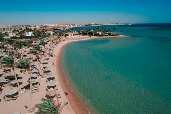 Luftaufnahme des Golden Beach Resorts mit Strand, Palmen, Sonnenschirmen und blauem Meer.