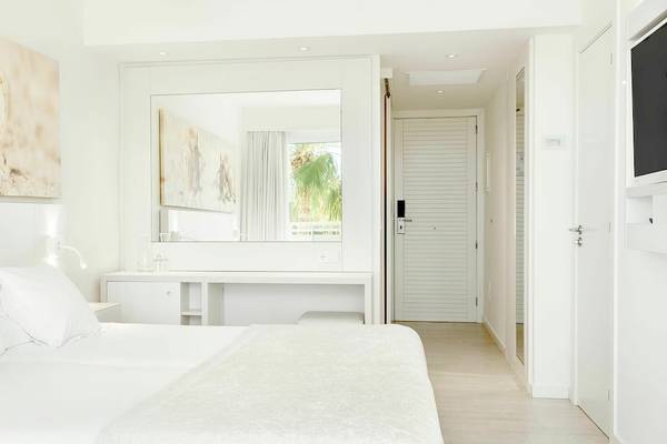 Innenansicht eines Schlafzimmers im Iberostar Cristina Hotel mit weißem Bett, Möbeln und Dekoration.