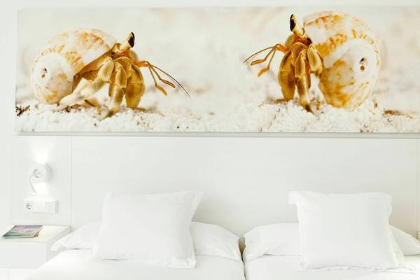 Hotelzimmer mit zwei Betten, weißen Kissen und Nachttischen, sowie einer Wand mit Meerestier-Bild.