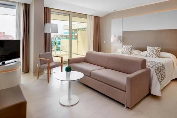 Innenansicht der Suite im Hotel Hipotels Gran Playa de Palma mit Bett, Sofa, Tisch und Fernseher.