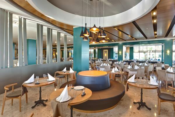 Innenansicht des Restaurants im Sherwood Dreams Resort mit runden und rechteckigen Tischen, hängenden Lampen und modernen Möbeln.