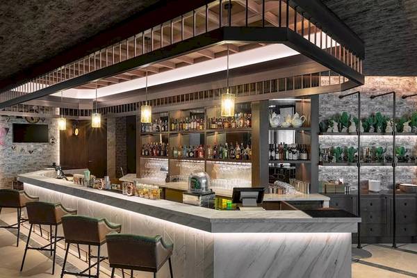 Innenansicht der Bar im Taj Exotica Resort & Spa The Palm Dubai mit einer Theke, Hockern und dekorativen Flaschen.