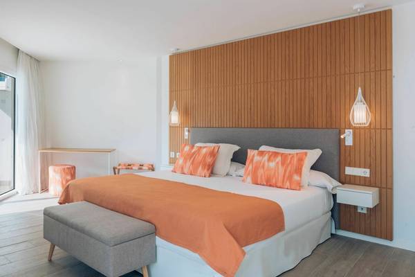 Schlafzimmer im Iberostar Playa de Muro Hotel mit Doppelbett, orange Bettwäsche, Nachttischen und begehbarer Dusche.