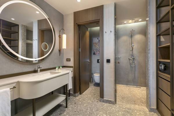 Badezimmer im Cullinan Belek Hotel mit ovalem Spiegel, Waschbecken und Dusche.