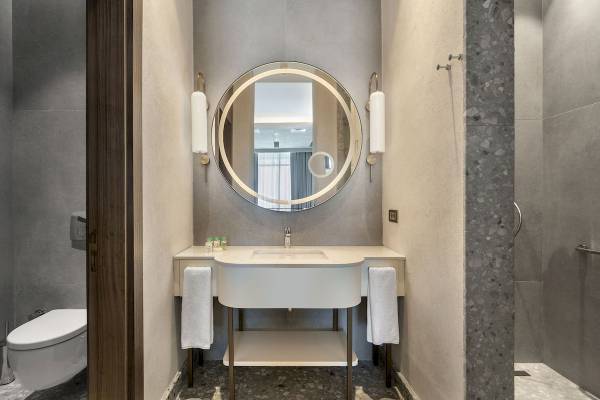 Badezimmer im Cullinan Belek Hotel mit runden Spiegel, weißer Waschbecken und Handtüchern.