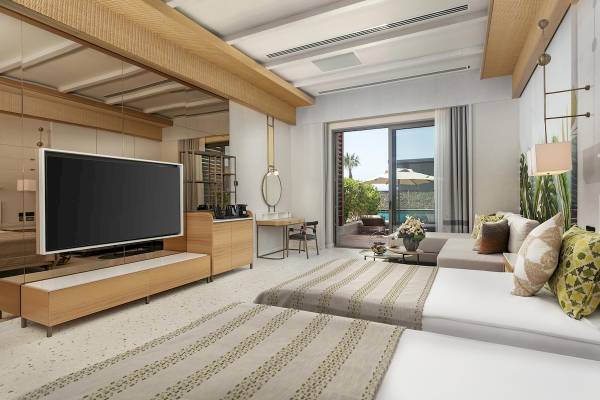 Innenansicht eines Gästezimmers im Cullinan Belek Hotel mit Fernseher, Schreibtisch und Poolblick.