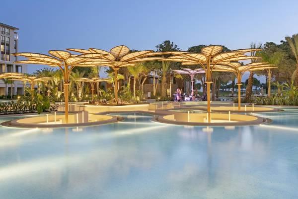 Abendlicher Pool im Cullinan Belek Hotel mit goldenen Schirmen und beleuchteten Pflanzen.