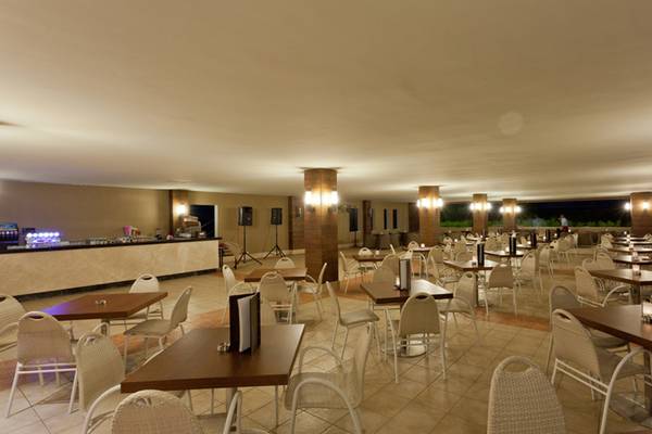 Innenbereich des Sherwood Dreams Resort Restaurants mit vielen Tischen und Stühlen, Beleuchtung und Bar im Hintergrund.