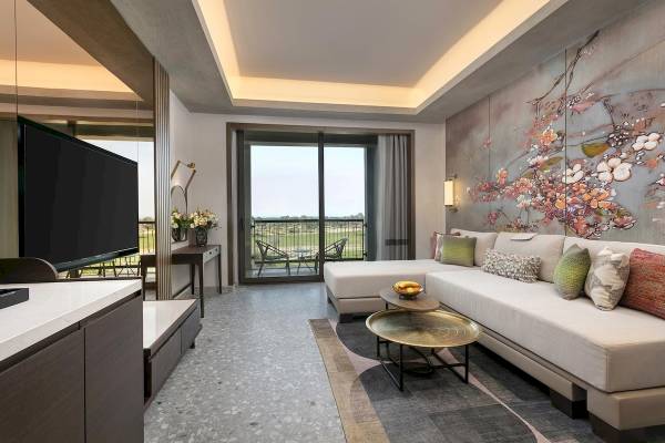 Cullinan Belek Hotel Wohnbereich mit Sofa, Fernseher und großem Fenster mit Blick auf die Landschaft.