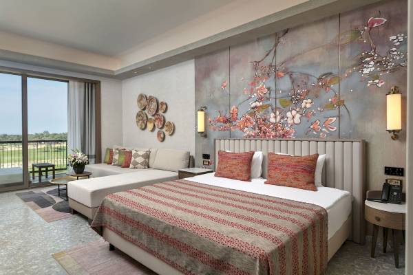Innenansicht des Cullinan Belek Hotelzimmers mit Bett, Sofa, Wanddekoration und Balkon.