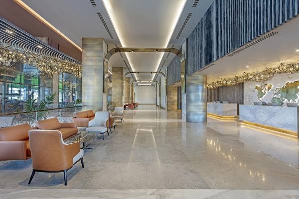 Lobbyansicht des Cullinan Belek Hotels mit Marmorboden, Ledersofas und einer Empfangstheke.