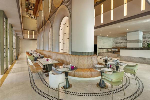 Innenbereich des Cullinan Belek Hotels mit gepolsterten Sitzbänken und runden Tischen.