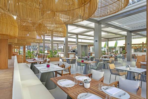 Innenbereich des Cullinan Belek Hotels mit vielen Tischen, Stühlen und hängenden Bambuslampen.