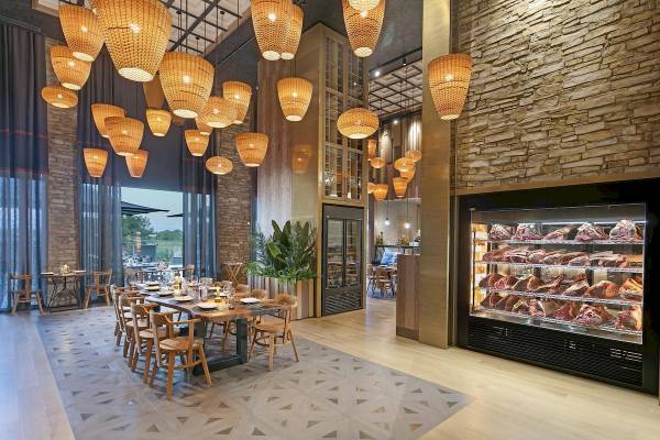 Innenraum des Cullinan Belek Hotels mit Esstisch, hölzernen Stühlen und rustikalem Design.
