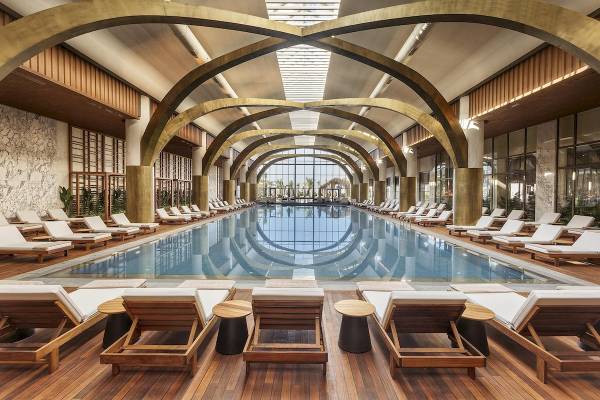 Innenpool des Cullinan Belek Hotels mit Loungestühlen und Glaswänden.