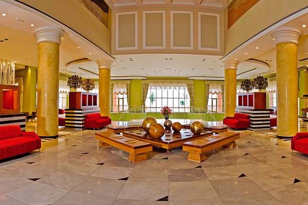 Lobby des Iberostar Selection Rose Hall Suites Hotels mit roten Sesseln und goldenen Tischen.