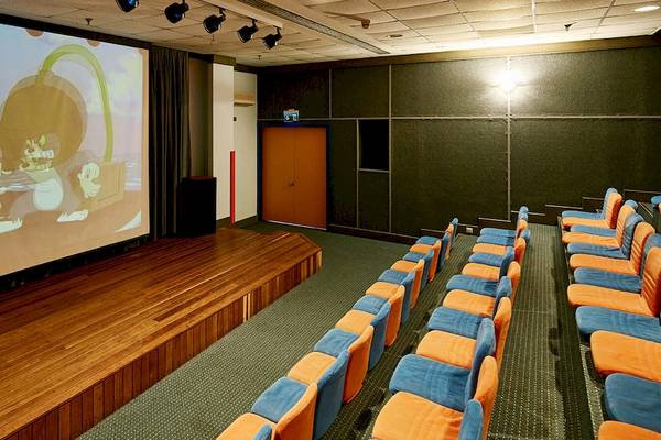 Kinossaal im Gloria Serenity Resort mit großen Leinwand und Reihen von orange und blauen Stühlen.