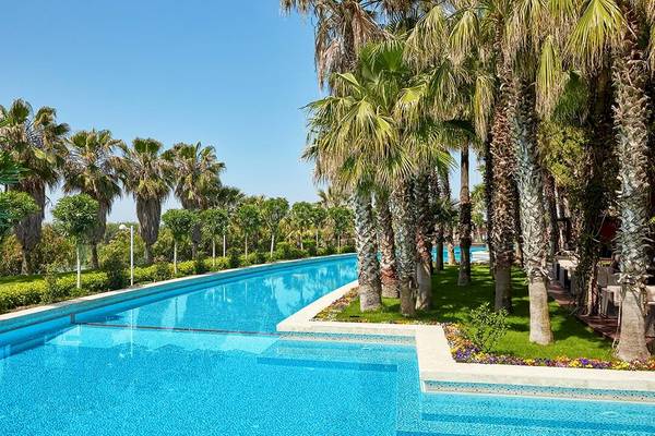 Ein großer Swimmingpool im Gloria Serenity Resort, umgeben von Palmen und grüner Rasenfläche.
