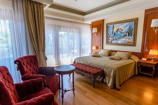 Schlafzimmer im Gloria Serenity Resort mit einem großen Bett, zwei roten Sesseln, einem Tisch und einem Gemälde an der Wand.
