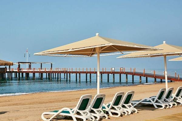 Strand des Gloria Golf Resorts mit Sonnenschirmen und Liegen vor einem Steg im Meer