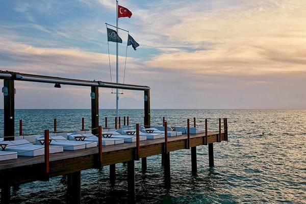 Terrasse am Meer im Gloria Golf Resort mit weißen Liegestühlen und Flaggen.