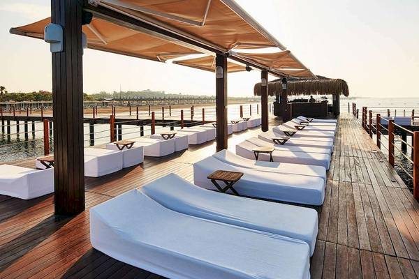 Lounge-Terrasse im Gloria Golf Resort mit weißen Liegestühlen und Sonnenschirmen am Meer