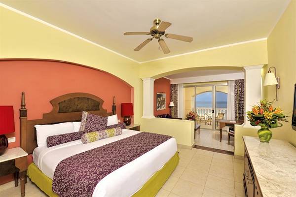 Hotelzimmer mit Bett, Deckenventilator, Tisch, Sessel, Balkon und Meerblick im Iberostar Selection Rose Hall Suites.