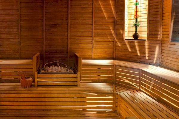 Innenansicht der Sauna im Gloria Golf Resort mit Holzbänken, offenen Fenstern und einer Holzkiste mit Steinen.