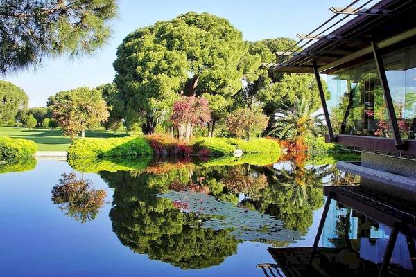 Außenansicht des Gloria Golf Resorts mit einem See, Bäumen und einem Gebäude