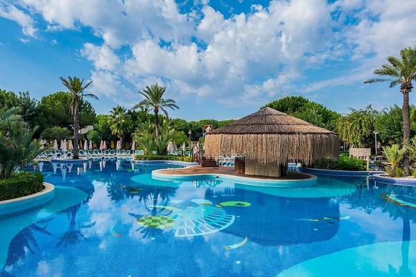 Außenpool des Gloria Golf Resorts mit einem Strohdach-Snackbar und umgeben von Palmen und Pflanzen.