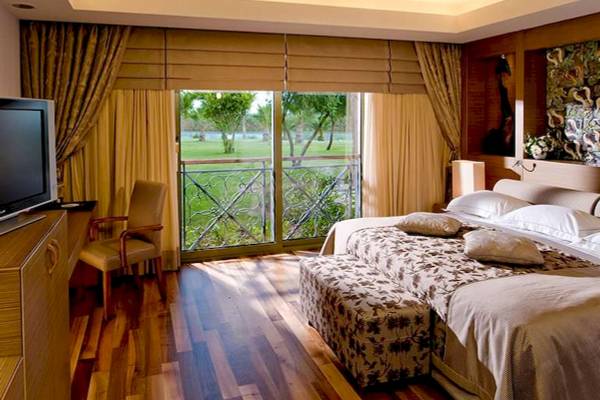 Hotelzimmer mit großem Bett, Fenstern und Ausblick auf Golfplatz