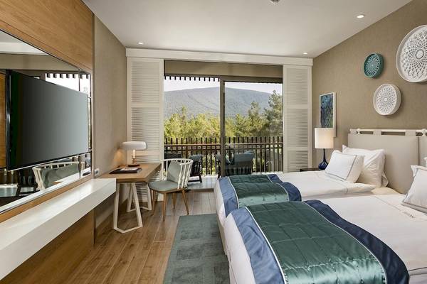 Zwei Betten mit Aussicht auf eine Terrasse und einen Berg im Titanic Luxury Collection Bodrum.