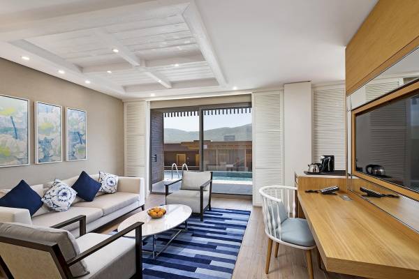Wohnbereich des Titanic Luxury Collection Bodrum Hotels mit Sofa, Stühlen und Fernseher.