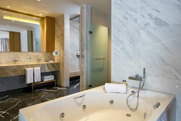 Modernes Badezimmer des Titanic Luxury Collection Bodrum mit Badewanne, Marmorwänden und Spiegel.