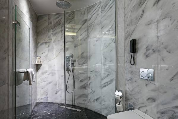Ein modernes Badezimmer im Titanic Luxury Collection Bodrum mit Marmorwänden und einer Glasdusche.
