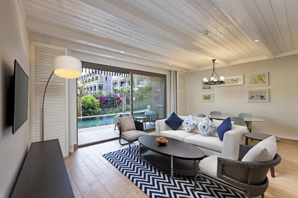 Wohnzimmer mit Sofa, Tisch, Fernseher und offenem Fenster zum Pool