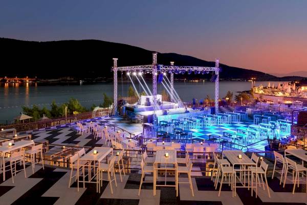 Abendveranstaltung auf der Terrasse des Hotels Titanic Luxury Collection Bodrum mit einer Bühne, blauen Lichtern und vielen Tischen und Stühlen.