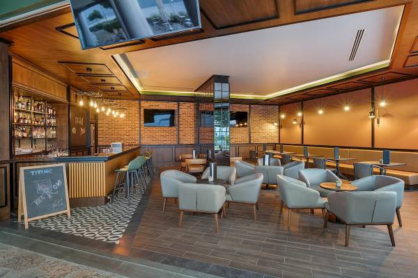 Innenansicht der Cocktail-Bar des Titanic Luxury Collection Bodrum Hotels mit Holzelementen, Sesseln und einer Tafel.