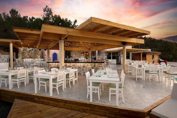 Außenterrasse des Titanic Luxury Collection Bodrum Hotels mit weißen Tischen und Stühlen unter einem Holzdach.